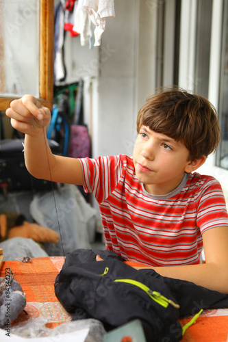 Billede på lærred preteen handsome boy sew hole in the torn trousers