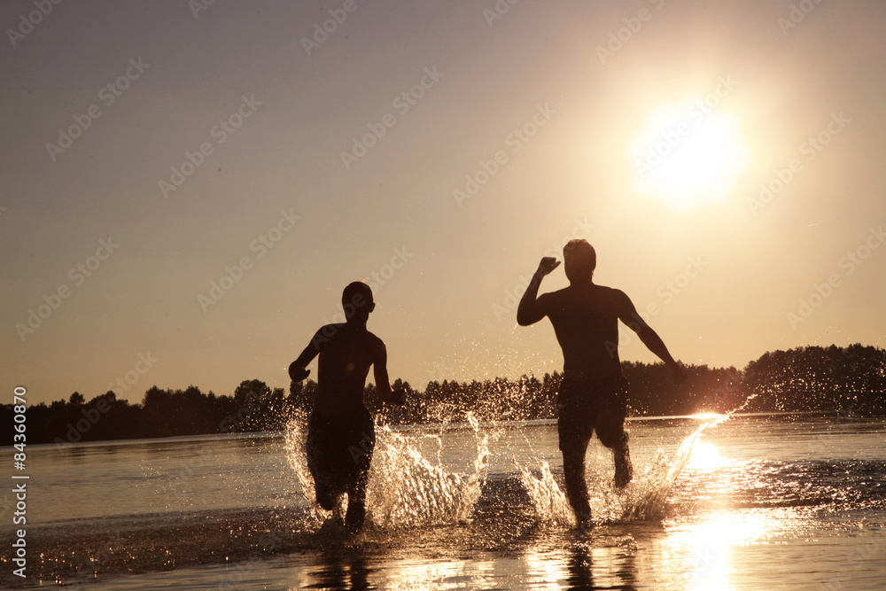 Fototapeta premium Glückliche junge Menschen laufen und springen am See beim Sonnenuntergang