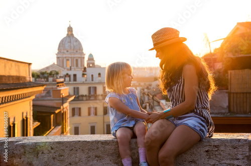Mother and daughter sitting on ledge at sunset in Rome