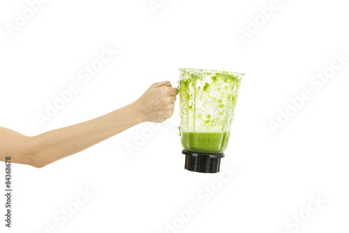 Arm holding a mixer jar filled with green smoothie