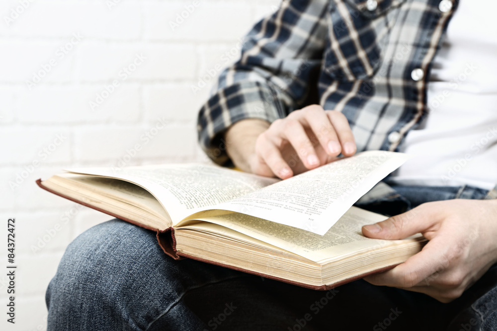 Young man reading book, close-up, on light background Young man reading book, close-up, on light background