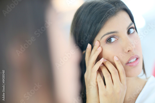 Beautiful brunette girl looking at skin in mirror