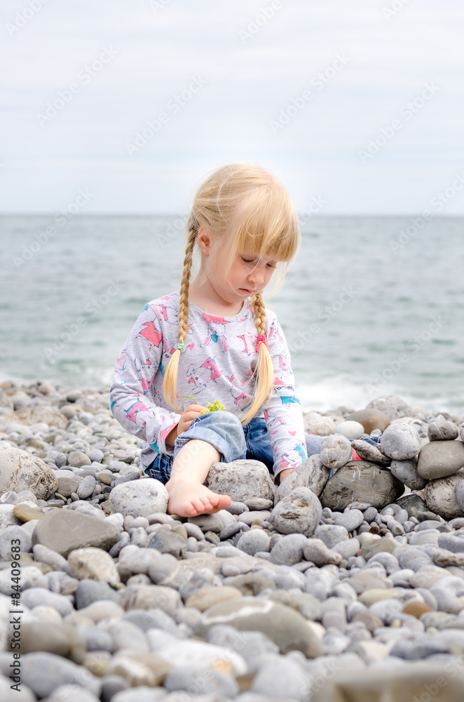 Blond Girl Building Stone Wall on Rocky Beach Blond Girl Building Stone Wall on Rocky Beach