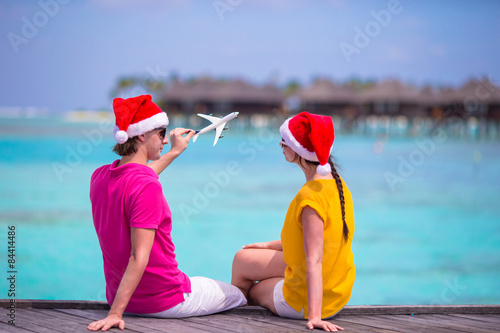 Young couple in Santa hats relaxing on wooden jetty on Christmas