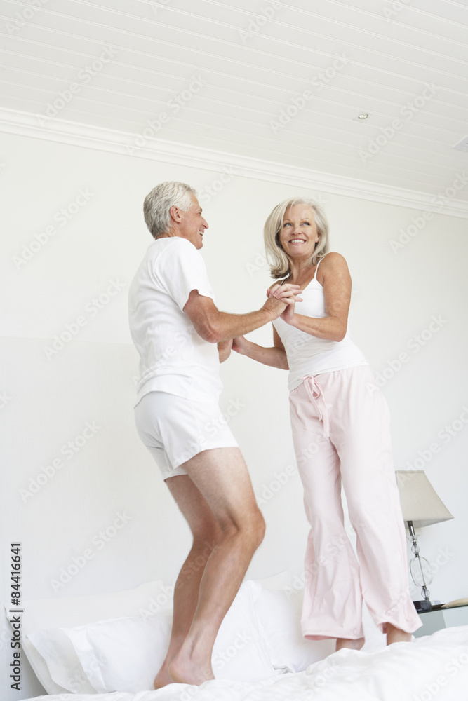 Fototapeta premium Senior Couple Jumping On Bed Wearing Pyjamas