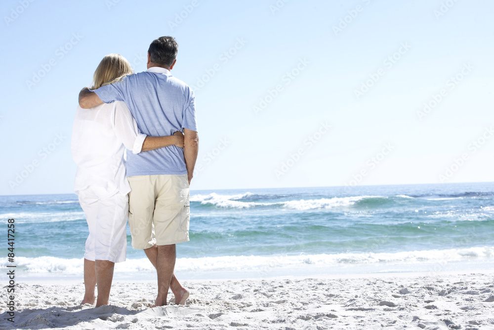 Senior Couple On Holiday Walking Along Sandy Beach Looking Out To Sea Senior Couple On Holiday Walking Along Sandy Beach Looking Out To Sea