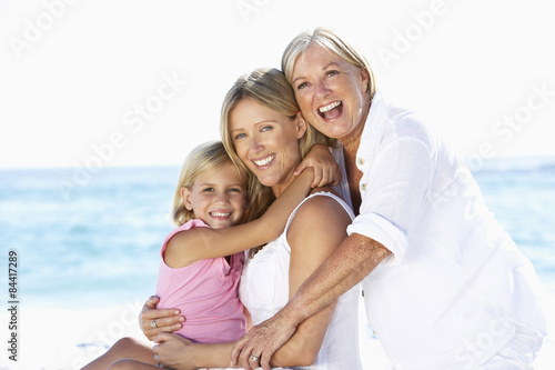Grandmother With Daughter And Granddaughter Embracing On Beach Holiday