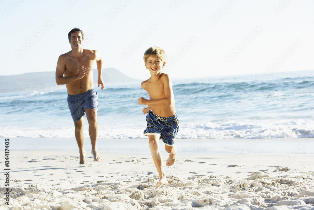 Father And Son On Holiday Running Along Beach