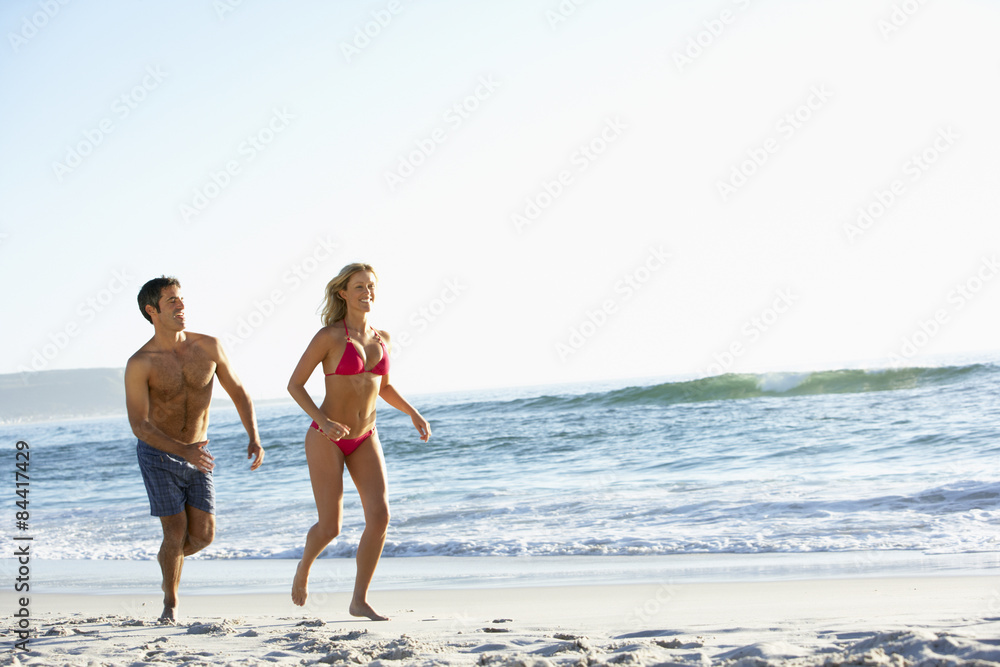 Young Couple Running Along Sandy Beach on Holiday