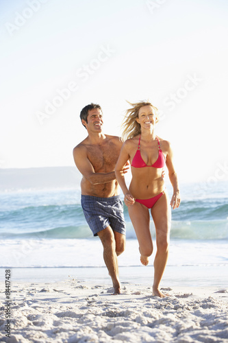 Young Couple Running Along Sandy Beach on Holiday © Monkey Business