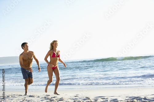 Young Couple Running Along Sandy Beach on Holiday © Monkey Business