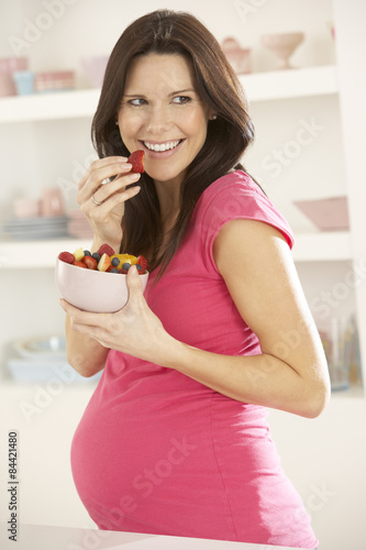 Pregnant Woman Eating Fruit Salad In Kitchen At Home