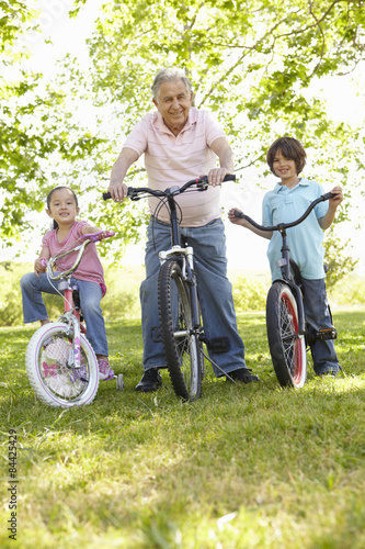 Hispanic Grandfather With Grandchildren In Park Riding Bikes