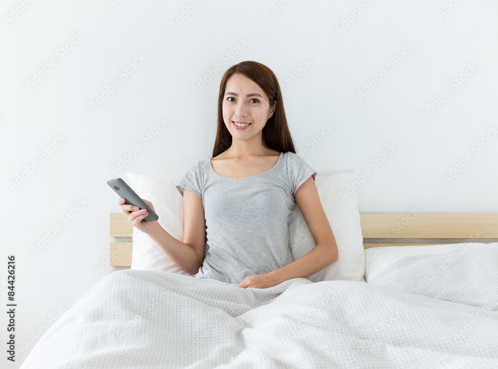 Asian woman holding the mobile phone and sitting on the bed Asian woman holding the mobile phone and sitting on the bed