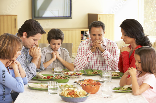 Extended Hispanic Family Saying Prayers Before Meal At Home