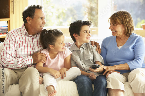 Hispanic Grandparents With Grandchildren Relaxing On Sofa At Home