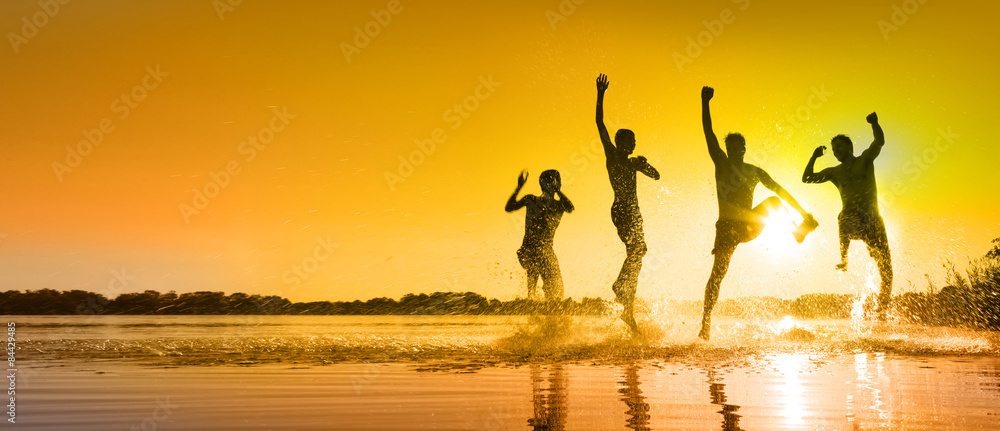Obraz premium Glückliche junge Menschen laufen und springen am See beim Sonnenuntergang