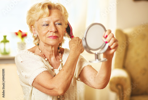 Foto Smiling elderly woman comb hair and looked in the mirror