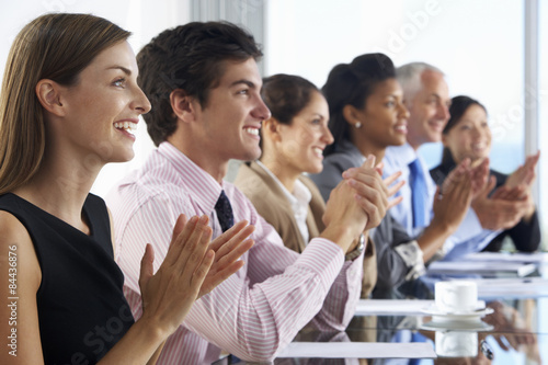 Line Of Business People Listening To Presentation Seated At Glass Boardroom Table