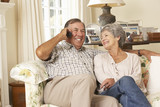 Retired Senior Couple Sitting On Sofa Talking On Phone At Home Together