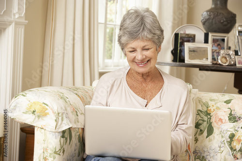 Retired Senior Woman Sitting On Sofa At Home Using Laptop