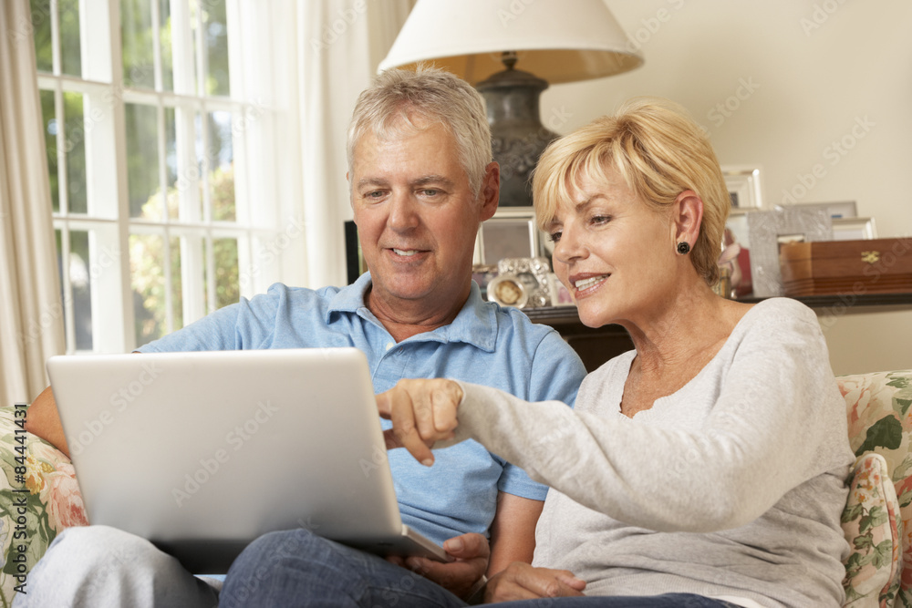 Mature Couple Sitting On Sofa At Home Using Laptop Mature Couple Sitting On Sofa At Home Using Laptop