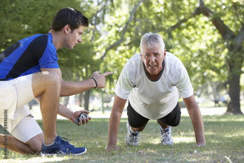 Fotografie Senior Man Working With Personal Trainer In Park
