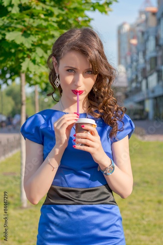 Beautiful girl is drinking coffee in front of buildings 
