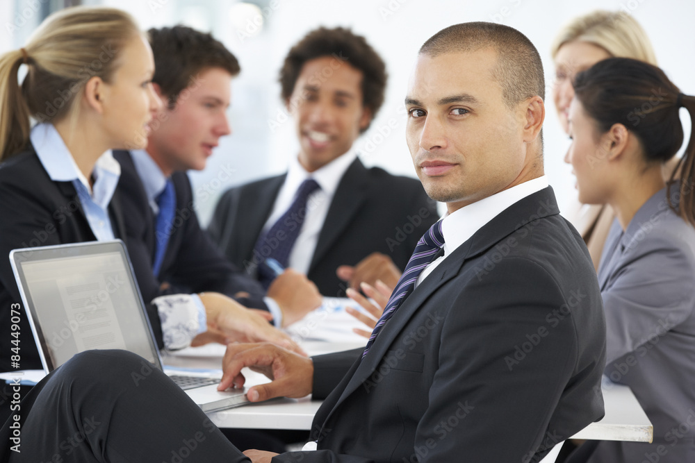 Portrait Of Male Executive With Office Meeting In Background Portrait Of Male Executive With Office Meeting In Background