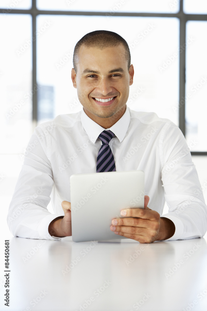 Businessman Sitting At Desk In Office Using Digital Tablet Businessman Sitting At Desk In Office Using Digital Tablet