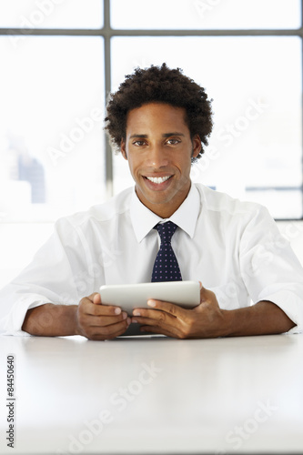 Businessman Sitting At Desk In Office Using Digital Tablet