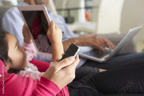 Family On Sofa With Smartphone, Laptop And Digital Tablet