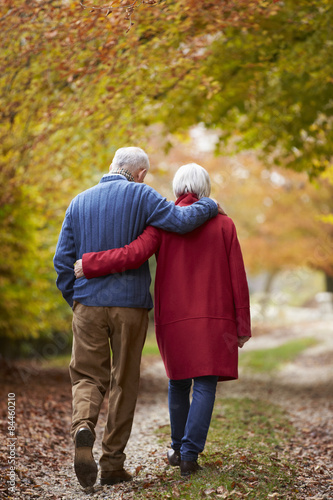 Rear View Of Senior Couple Walking Along Autumn Path