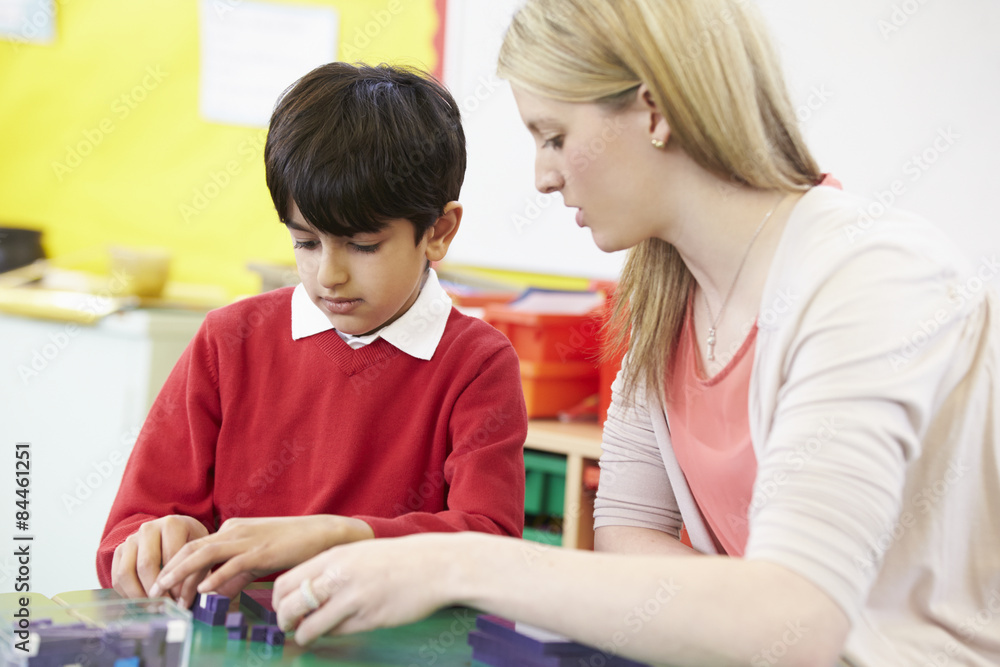 Teacher Helping Male Pupil With Maths At Desk Teacher Helping Male Pupil With Maths At Desk