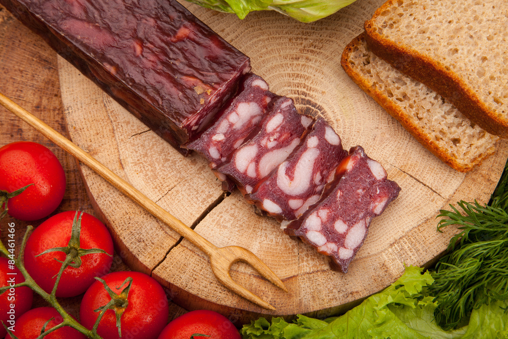Smoked meat sausage salami with bright summer vegetables and bread on wooden background