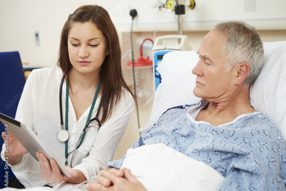 Obraz premium Doctor Sitting By Male Patient's Bed Using Digital Tablet