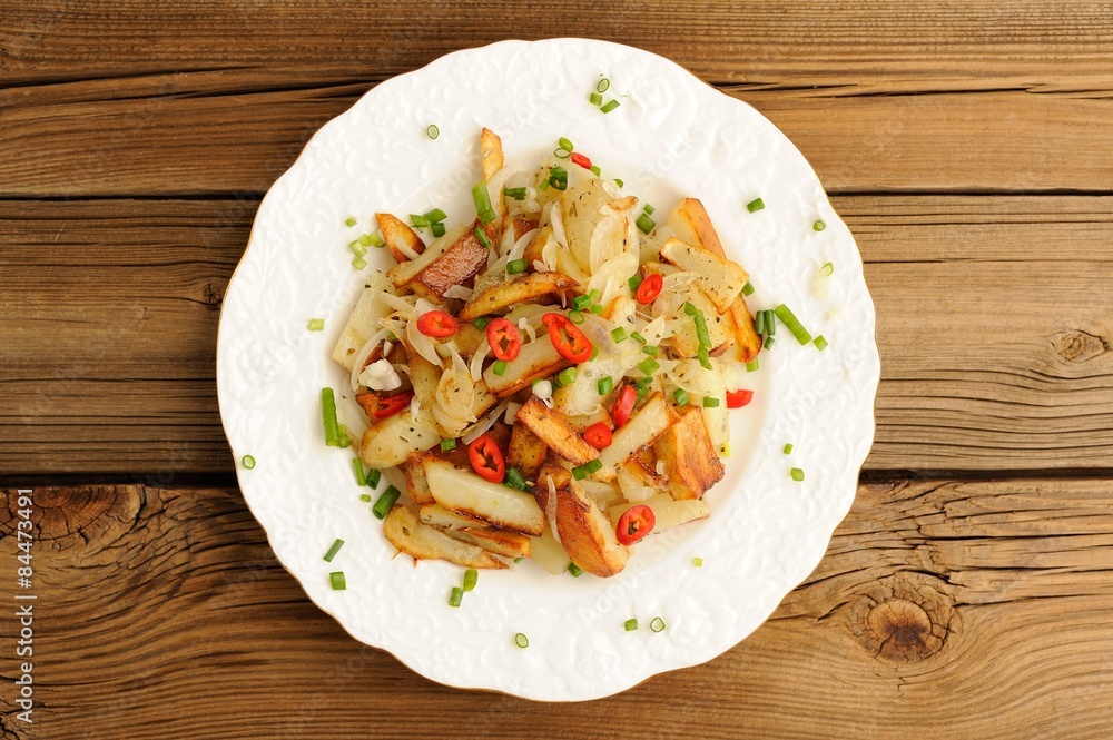 Fried potatoes with scallion and chili in white plate on wooden Fried potatoes with scallion and chili in white plate on wooden