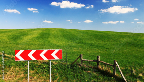 Green field with clouds, blue sky and road sign