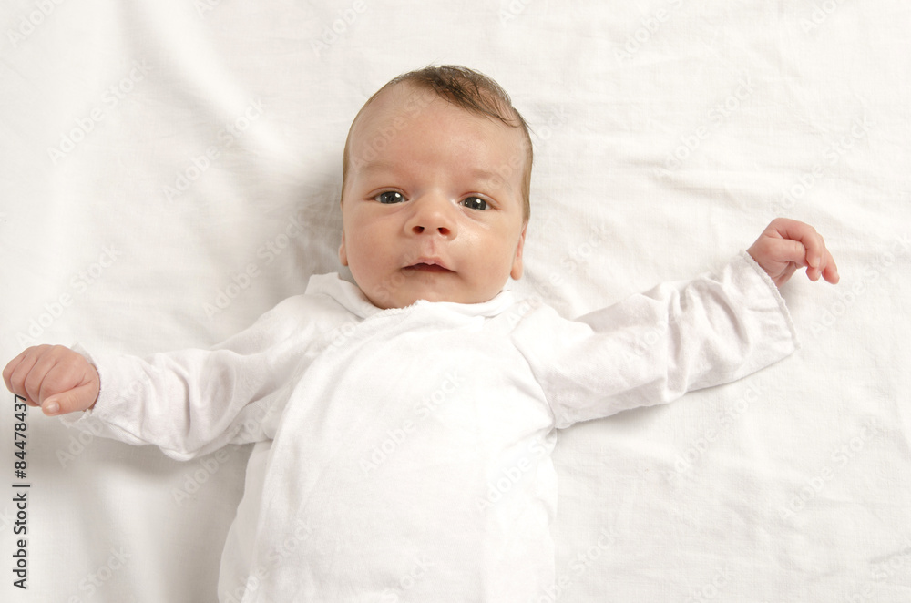 Beautiful innocent new born dressed in white looking at you. Adorable little boy relaxing in white sheets after a bath Beautiful innocent new born dressed in white looking at you. Adorable little boy relaxing in white sheets after a bath