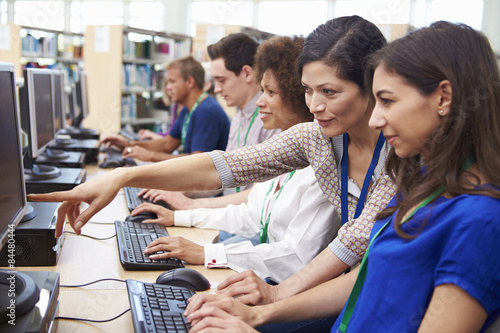 Group Of Mature Students Working At Computers With Tutor