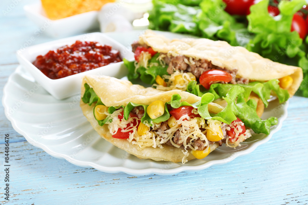 Tasty taco with tomato dip on plate and vegetables on table close up Tasty taco with tomato dip on plate and vegetables on table close up