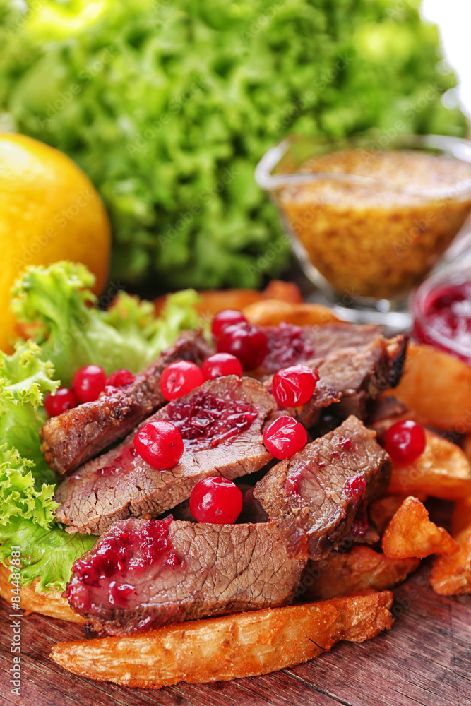 Beef with cranberry sauce, roasted potato slices and bun on wooden cutting board, close-up