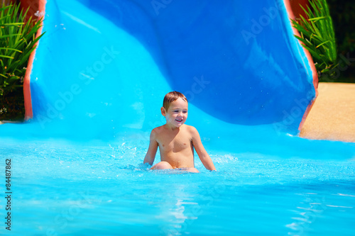 happy kid boy sliding in tropical water park