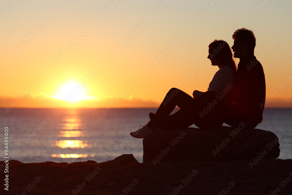 Couple silhouette sitting watching sun at sunset