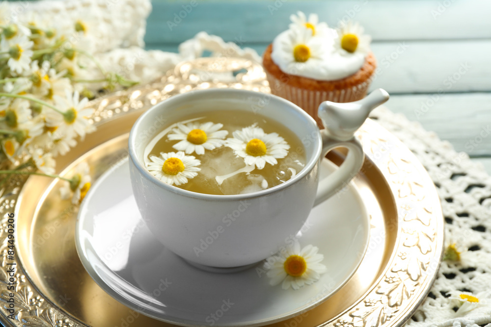 Cup of chamomile tea with chamomile flowers and tasty muffins on tray, on color wooden background Cup of chamomile tea with chamomile flowers and tasty muffins on tray, on color wooden background
