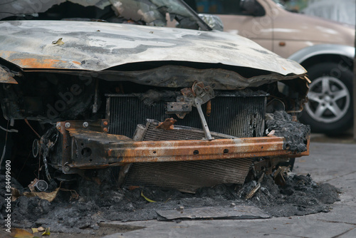 front of a burnt out car in an outdoor park