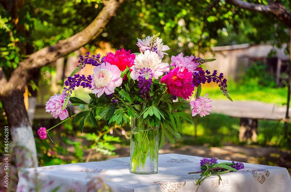 Beautiful bouquet of peonies and lupine on the table in the gree