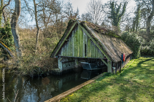 Run down thatched boathouse on Norfolk Broads surrounded by tree © capturelight