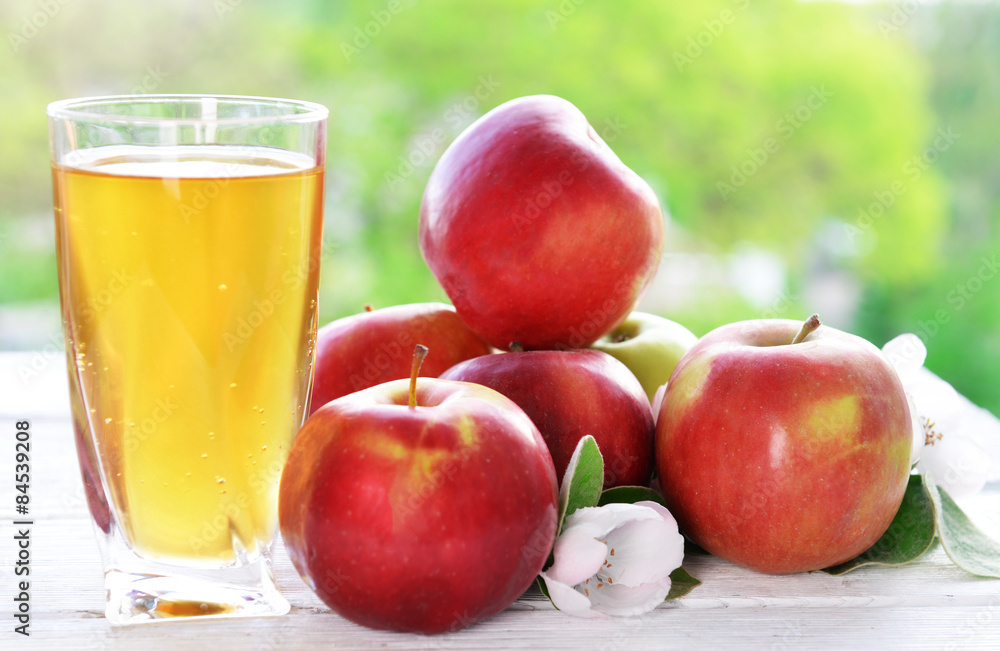 Glass of apple juice and apples on wooden table, on nature background Glass of apple juice and apples on wooden table, on nature background