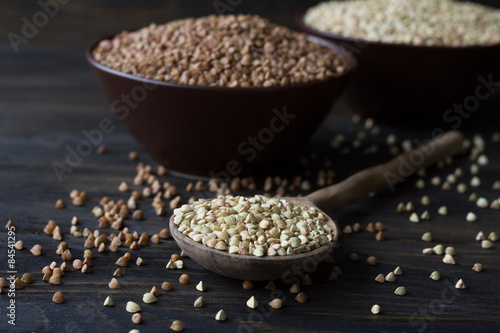 Green and brown buckwheat in ceramic bowls on a wooden surface